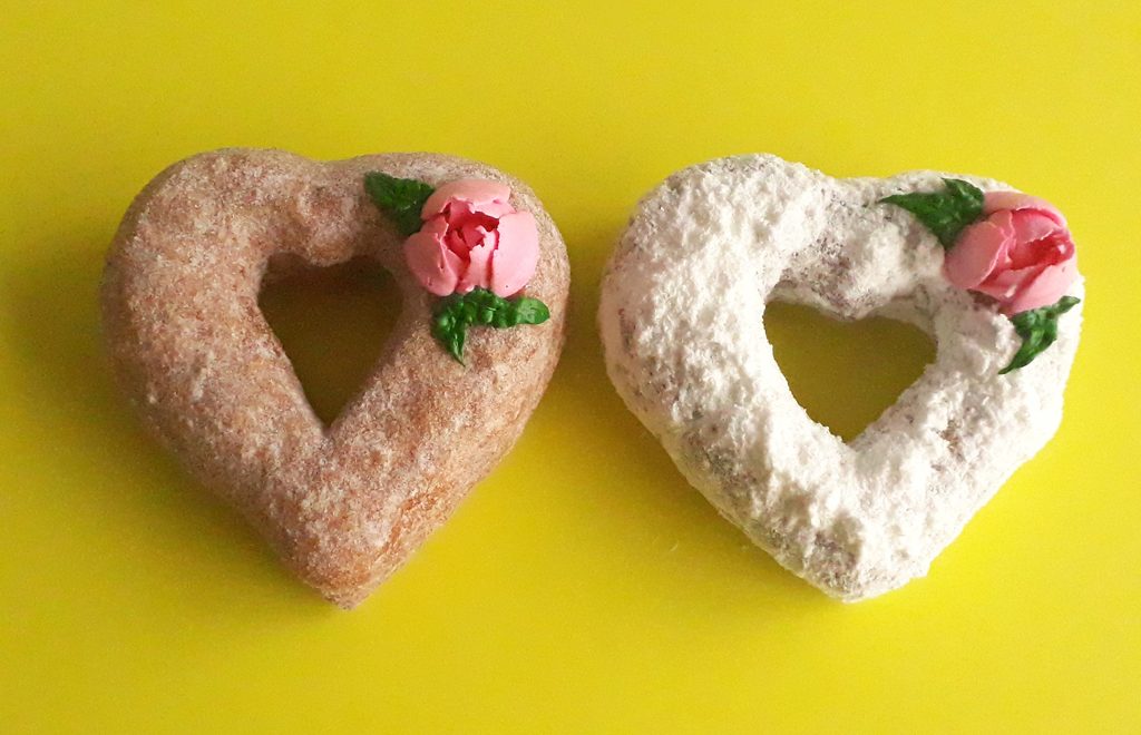 A beautifully crafted Valentine’s Powdered Sugar Croissant Cupid Donut, dusted with fine powdered sugar, topped with a delicate candy rose, and pierced with a strawberry cream Pocky stick as Cupid’s arrow. A crispy, flaky croissant donut perfect for Valentine’s Day.