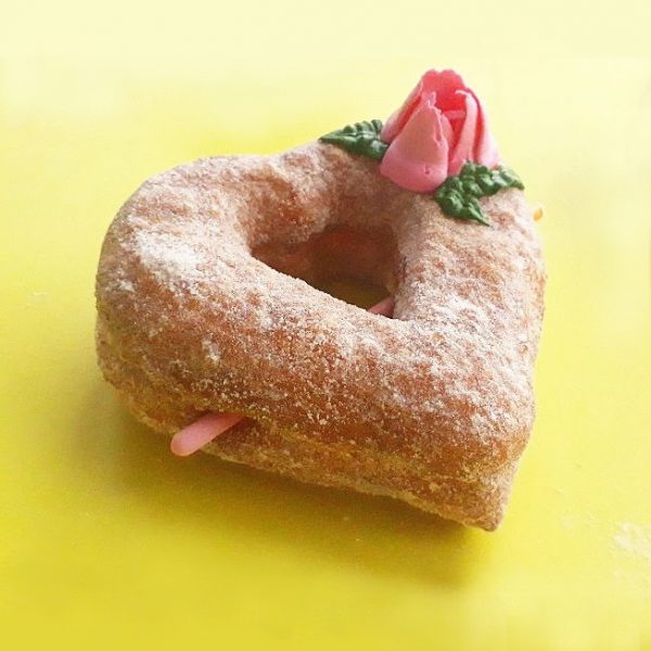 A beautifully crafted Valentine’s Croissant Cupid Heart Donut, dusted with fine sugar, topped with a delicate candy rose, and pierced with a strawberry cream Pocky stick as Cupid’s arrow. A crispy, flaky croissant donut perfect for Valentine’s Day.