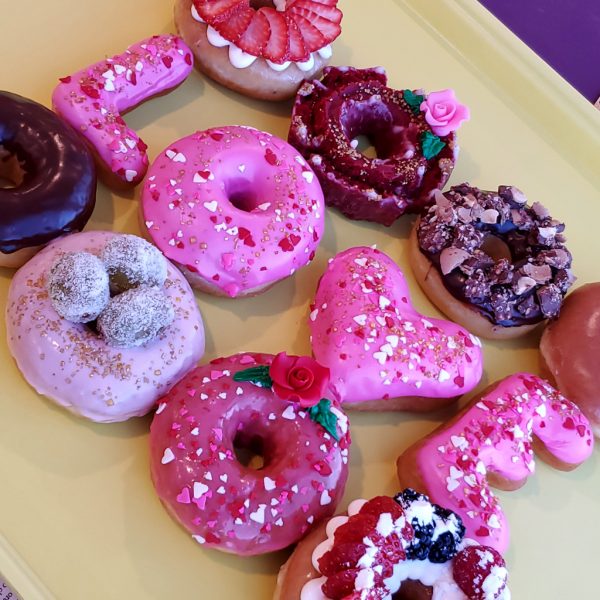 A beautifully decorated Valentine’s Pink Rose Heart Donut, coated in smooth pink icing, sprinkled with heart-shaped sprinkles, gold star accents, and edible gold sprinkles, and topped with a delicate candy rose. A perfect romantic treat for Valentine’s Day.