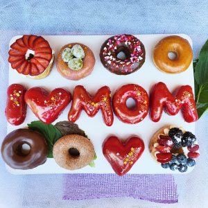 Mother’s Day donut gift set with “I ❤️ MOM” strawberry mirror glaze letter donuts, rosé champagne grape donut, strawberry cream cheese donut, and mixed berry cream cheese donut.
