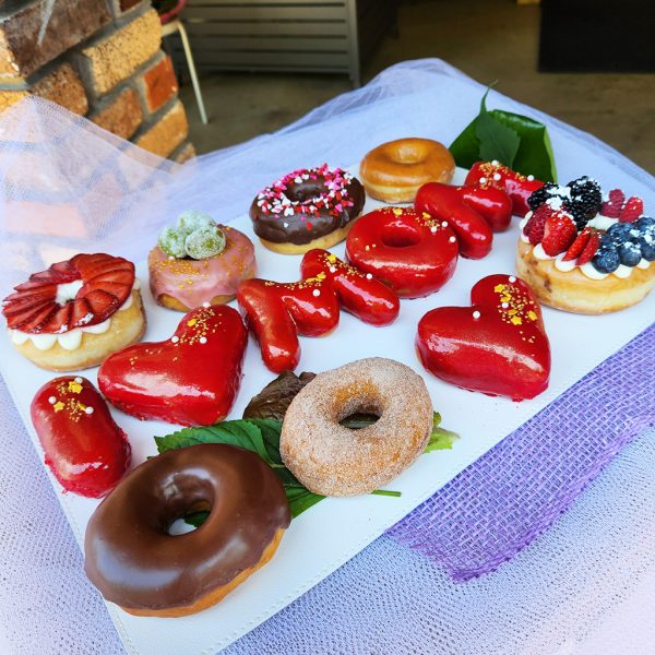 Mother’s Day donut gift set with “I ❤️ MOM” strawberry mirror glaze letter donuts, rosé champagne grape donut, strawberry cream cheese donut, and mixed berry cream cheese donut.