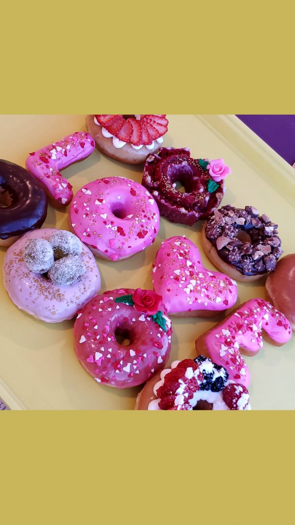 A beautifully decorated Valentine’s Pink Rose Heart Donut, coated in smooth pink icing, sprinkled with heart-shaped sprinkles, gold star accents, and edible gold sprinkles, and topped with a delicate candy rose. A perfect romantic treat for Valentine’s Day.