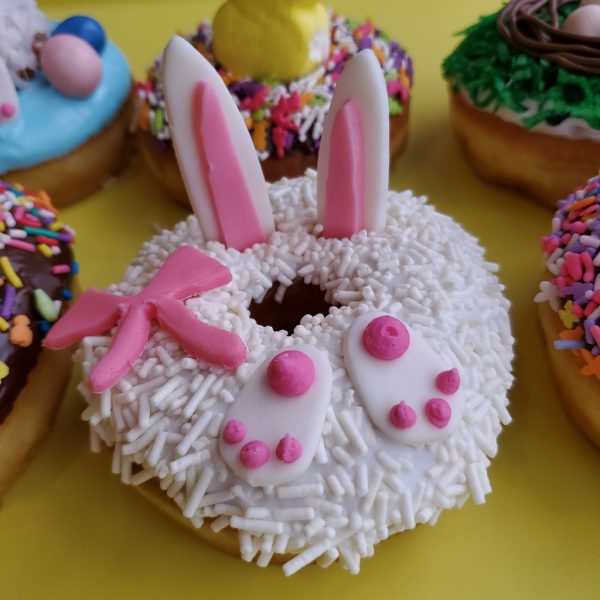 Easter donut decorated with bunny ears, pink paws, and a bow on a white sprinkle coating