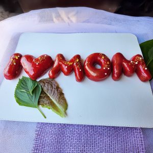 Strawberry mirror glaze donuts spelling “I ❤️ MOM,” decorated with edible gold powder, sugar pearls, and gold sprinkles for Mother’s Day.