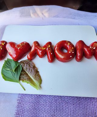 Strawberry mirror glaze donuts spelling “I ❤️ MOM,” decorated with edible gold powder, sugar pearls, and gold sprinkles for Mother’s Day.