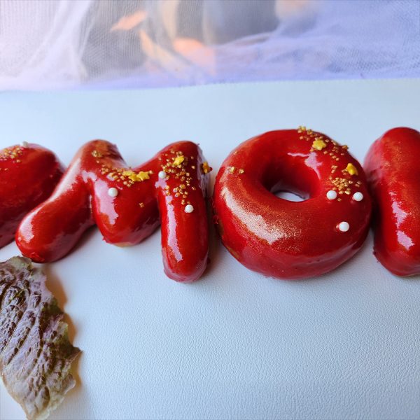 Strawberry mirror glaze donuts spelling “I ❤️ MOM,” decorated with edible gold powder, sugar pearls, and gold sprinkles for Mother’s Day.