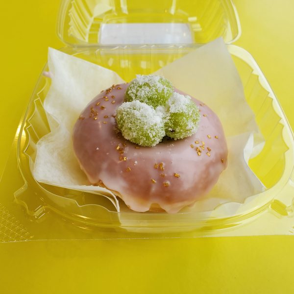 Rosé champagne glazed donut topped with sugar-coated green grapes infused with rosé, presented in a white bakery box.