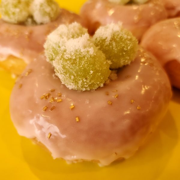 Rosé champagne glazed donut topped with sugar-coated green grapes infused with rosé, presented in a white bakery box.
