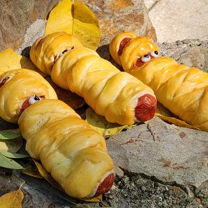 Savory kolache sausage rolls wrapped in dough and cheese to look like a festive Halloween mummy.