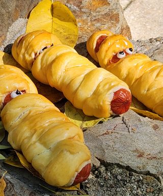 Savory kolache sausage rolls wrapped in dough and cheese to look like a festive Halloween mummy.