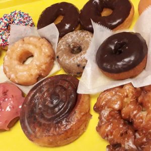 A yellow box filled with 1 Dozen Baker's Mix classic donuts from Jarams Donuts
